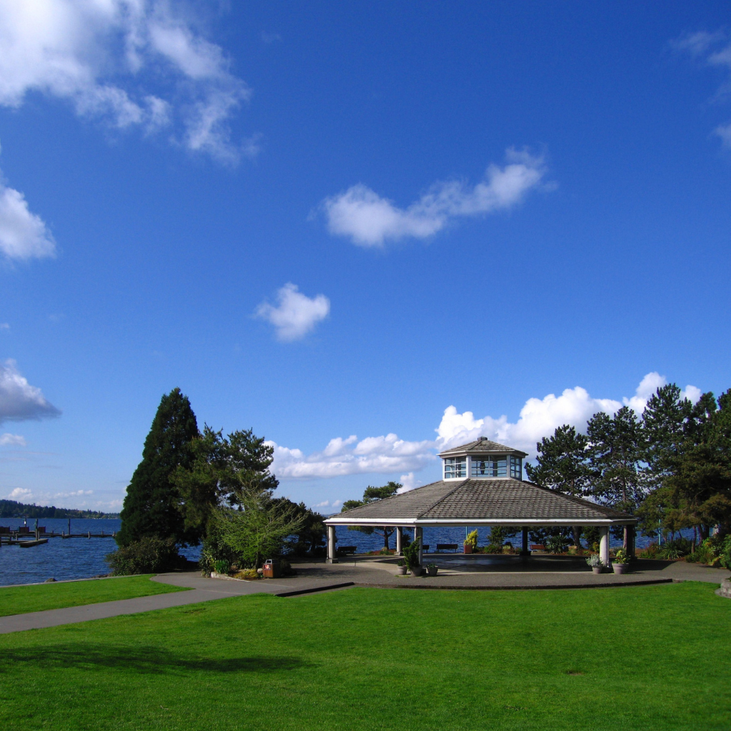 Scenic waterfront park with a gazebo, green lawn, trees, and blue sky with clouds