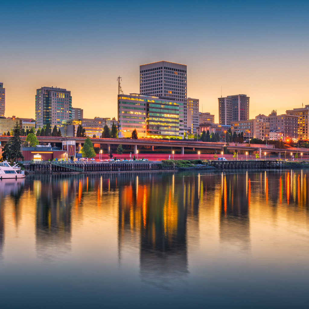 City skyline of Oakland, California at sunset with building lights reflecting on the water